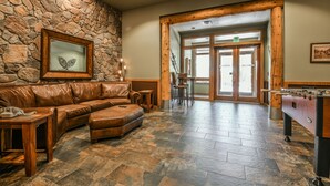 A lobby with a stone wall, a leather sofa, a wooden coffee table, a foosball table, and a framed picture.