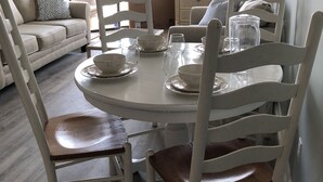 Un comedor con una mesa redonda, sillas blancas y un sofá al fondo.