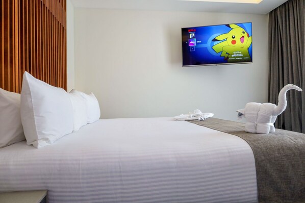 Ein Hotelzimmer mit Bett, Kissen, einem Fernseher, der einen Zeichentrickcharakter zeigt, einem Handtuch und einem Stofftier.