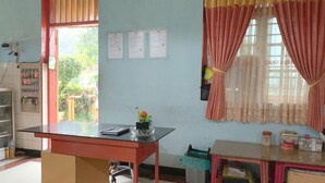 A classroom with a desk, chairs, a bookshelf, and a window with curtains.