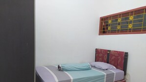 A single bed with a patterned headboard, a window with decorative grills, and a plain wall.