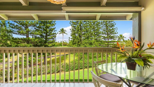 A balcony with a glass table and chairs, overlooking a well-maintained garden with trees and a golf course.