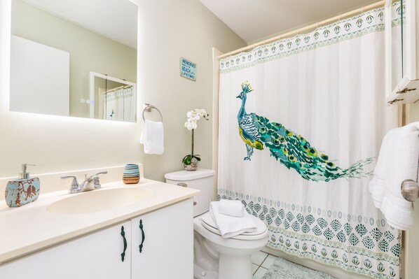 Un baño con lavamanos blanco, inodoro y cortina de ducha con diseño de pavo real.