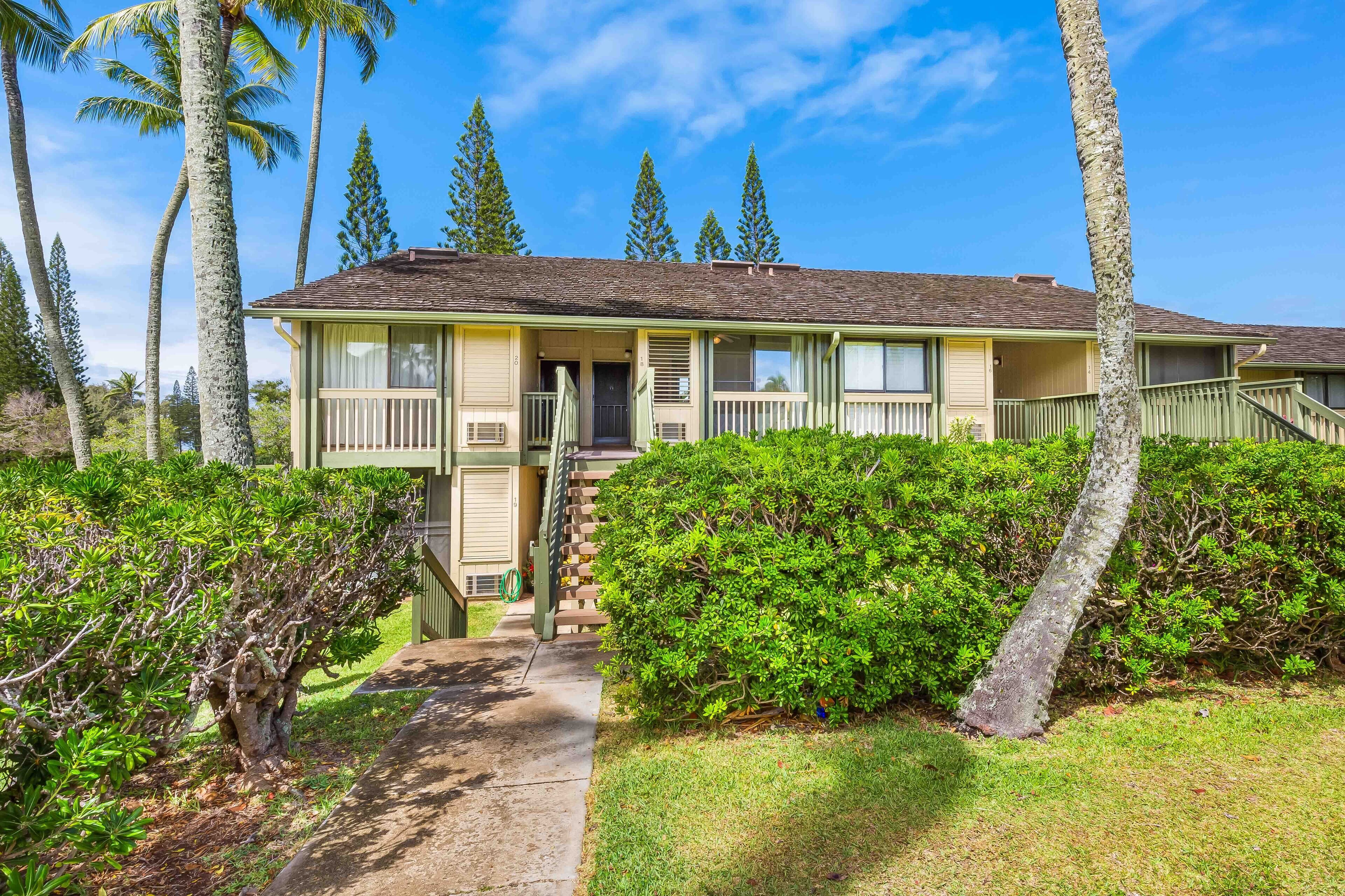 A two-story house with a front porch, surrounded by lush greenery and tall trees.