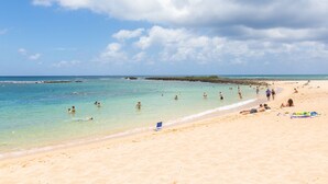 A beach with clear turquoise water, people swimming and sunbathing, and a sandy shore.
