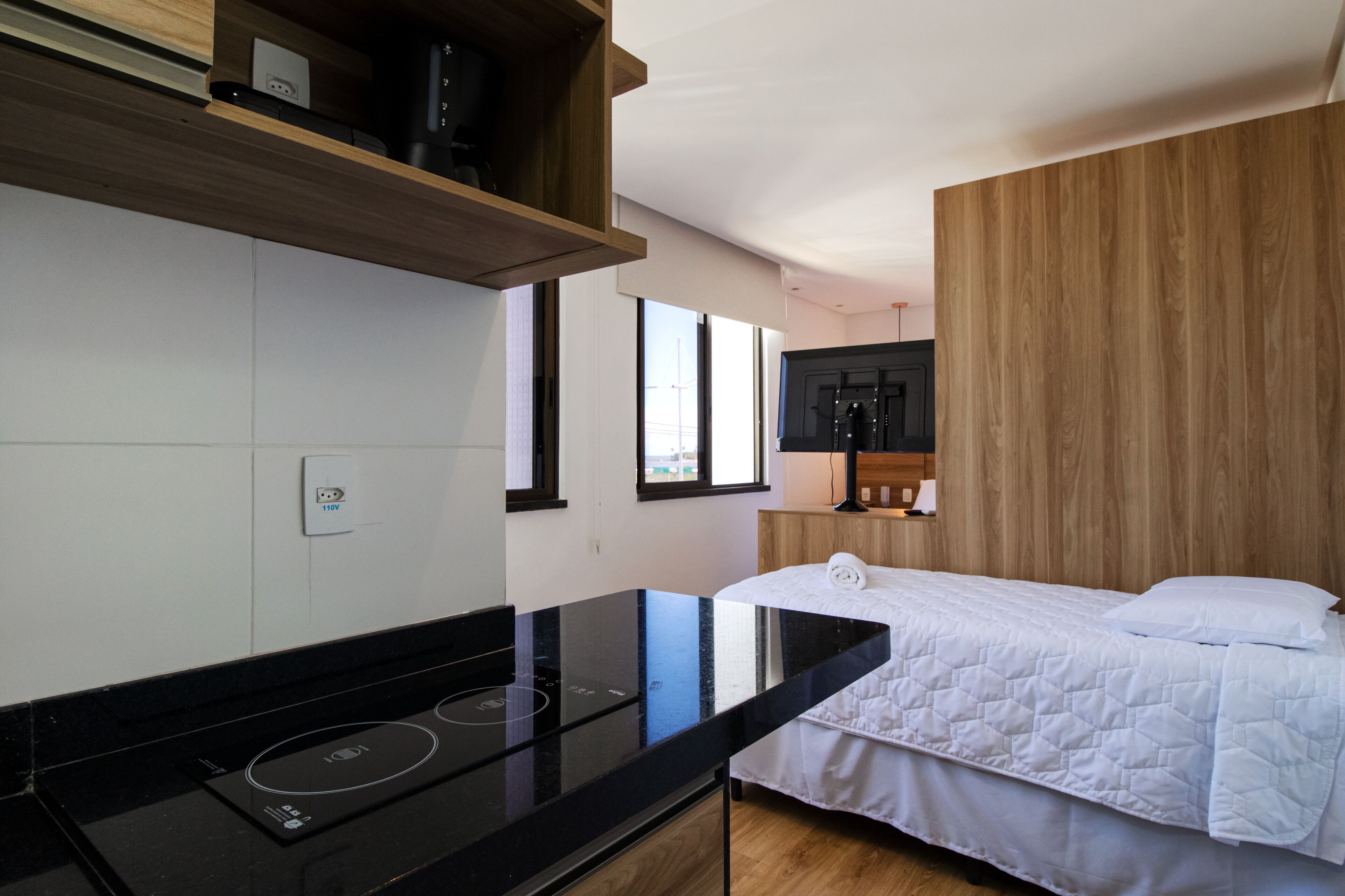 A modern kitchen with a black countertop and stove, a bed with white bedding, and wooden paneling on the walls.