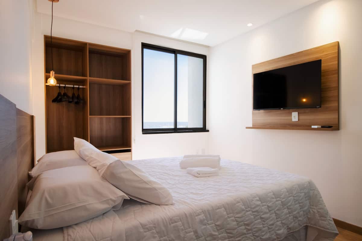 A bedroom with a bed, a TV mounted on the wall, a wardrobe, and a window.