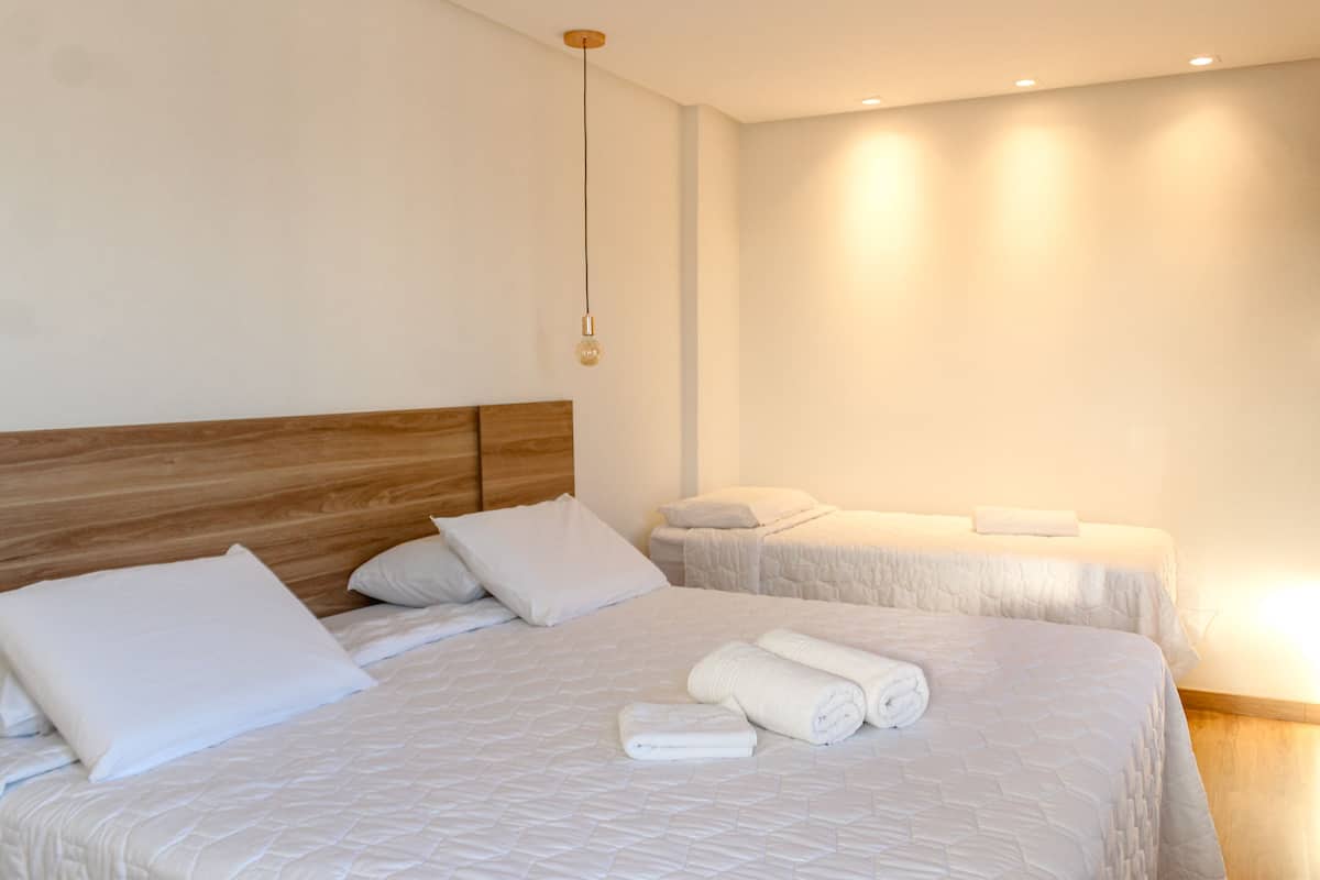 A hotel room with two beds, each with white bedding and pillows, a wooden headboard, and a hanging light fixture.
