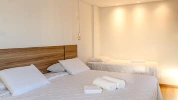 Habitación de hotel con dos camas, cada una con ropa de cama y almohadas blancas, un cabecero de madera y una lámpara colgante.