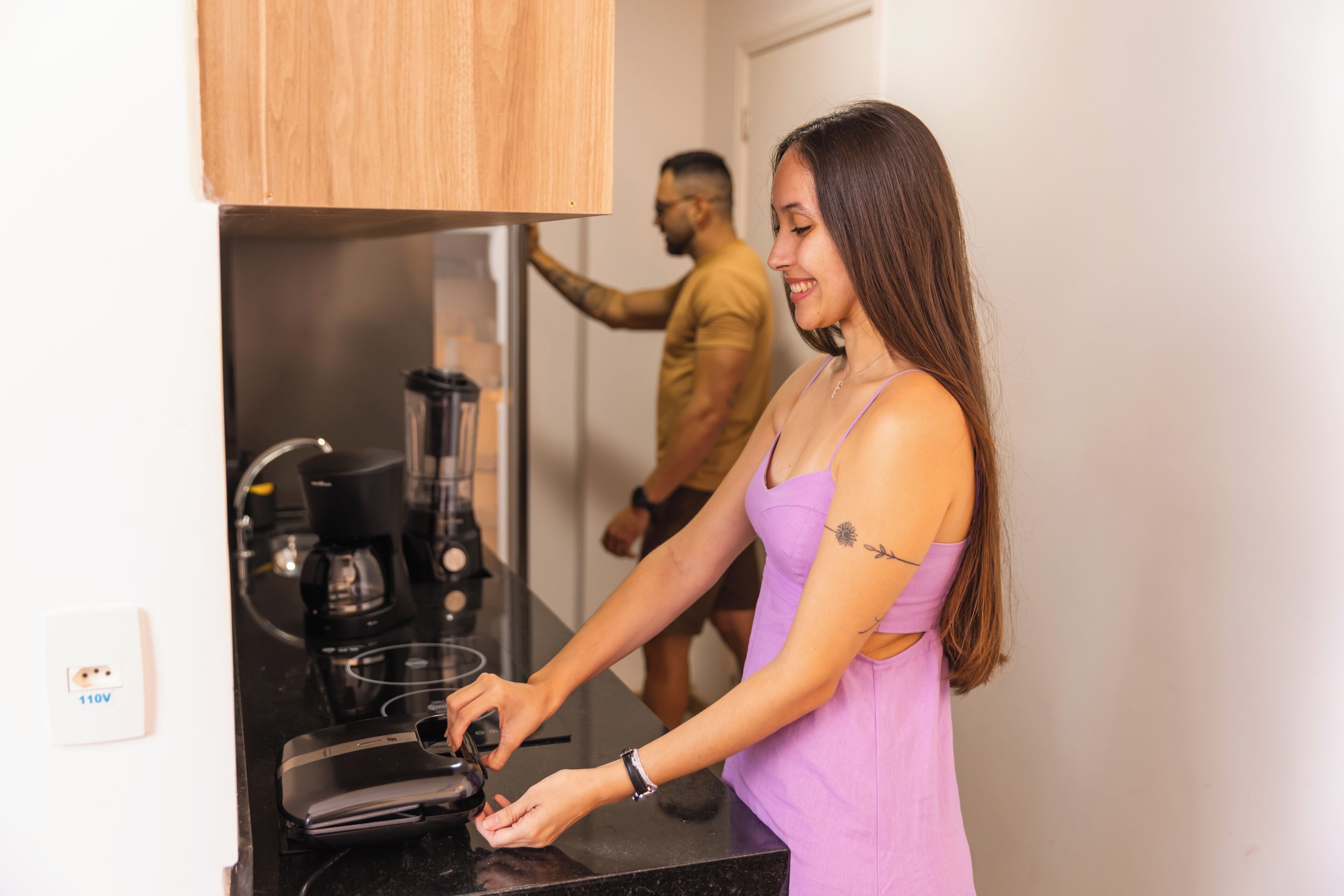 A woman in a purple dress preparing food at a kitchen counter with a coffee maker and blender.