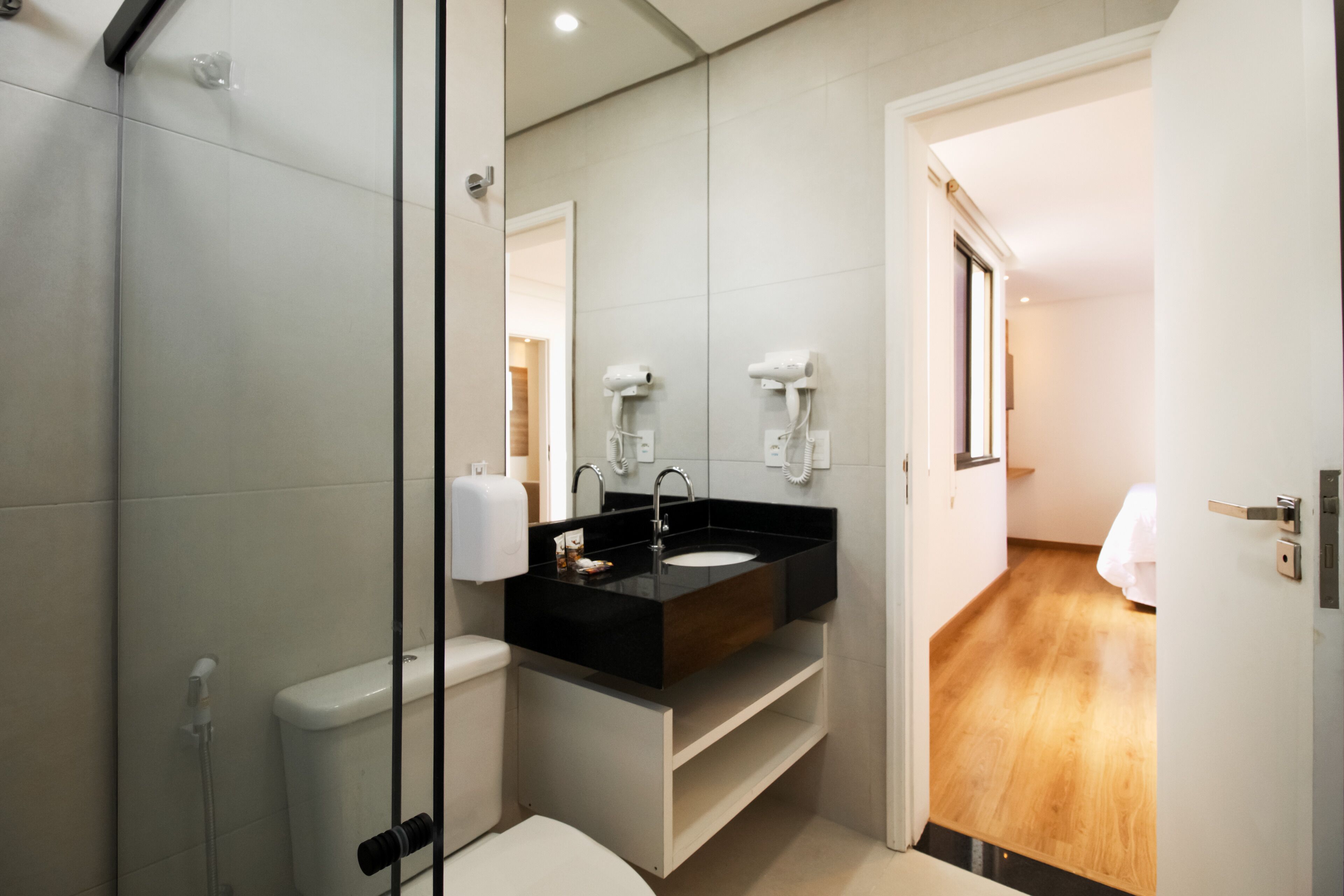 Une salle de bain moderne avec un lavabo noir, des toilettes blanches et une douche à l’italienne en verre.