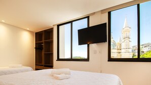 Habitación de hotel con una cama grande, un televisor montado en la pared y vista a una iglesia por la ventana.