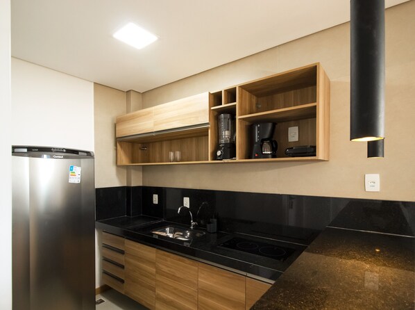 Una cocina moderna con refrigerador de acero inoxidable, encimera negra, armarios de madera y electrodomésticos integrados.