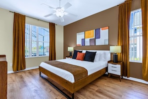 Een hotelkamer met een groot bed, twee nachtkastjes, een plafondventilator en een raam met gordijnen.