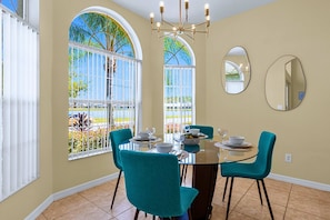 A dining area with a round table, teal chairs, and a view of palm trees through large windows. - Upstay: Crystal Cove Resort Villa w/ Pool & Games (Kissimmee)