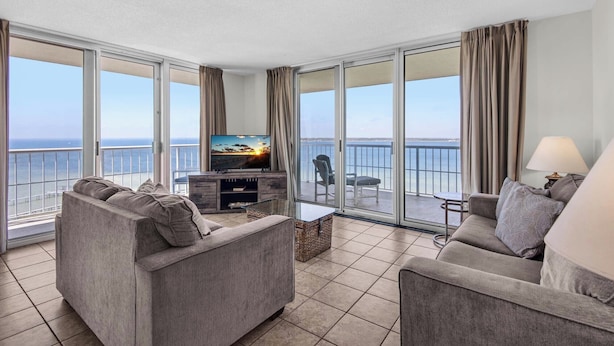 Een ruime woonkamer met een grote televisie, comfortabele zithoek en een balkon met uitzicht op zee.