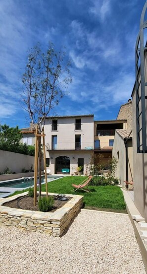 A modern building with a pool, a small garden, and a clear blue sky.
