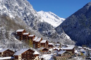 A mountain resort with chalet-style lodges, a ski lift, and snow-covered mountains.