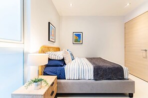 A modern bedroom with a bed, bedside table, lamp, and two framed pictures on the wall.