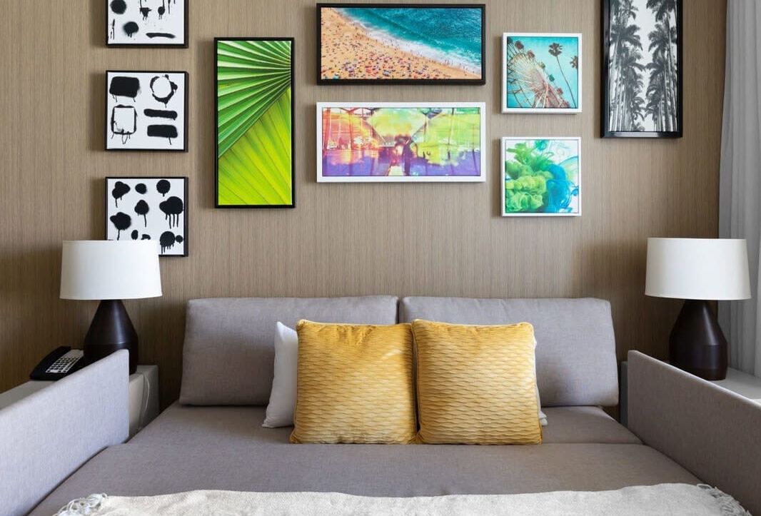 A hotel room with a bed, two bedside lamps, and a wall decorated with various framed artworks.