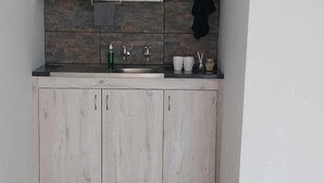 A small kitchen with light wood cabinets, a black kettle on the countertop, and a black towel hanging on a rack. - Sweetafrica lodge (Hartbeespoort)