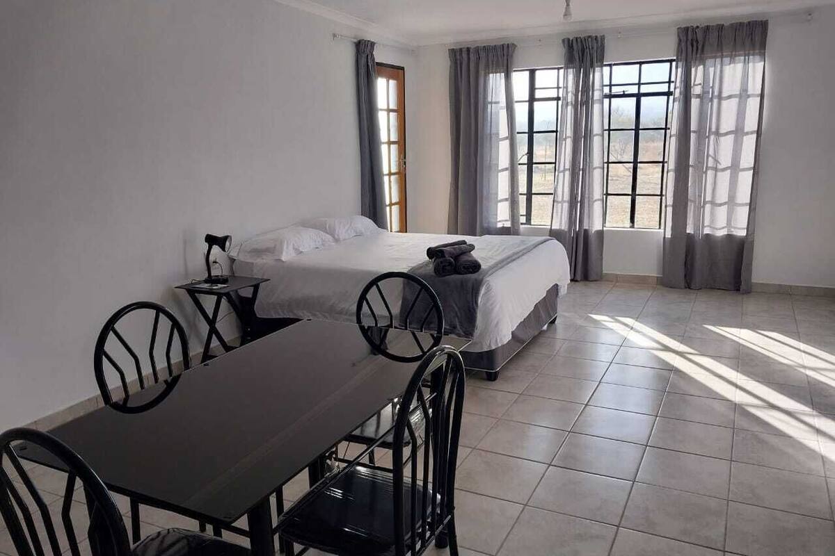 A hotel room with a bed, a dining table with chairs, and a window with curtains.