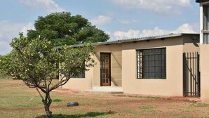 A single-story building with a beige exterior, a wooden door, and a window with black bars. - Sweetafrica lodge (Hartbeespoort)