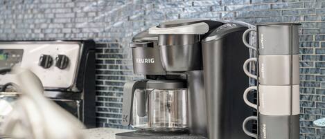 Une machine à café Keurig avec un porte-tasse à café à côté, posée sur un comptoir de cuisine dont le mur arrière est recouvert de carreaux.