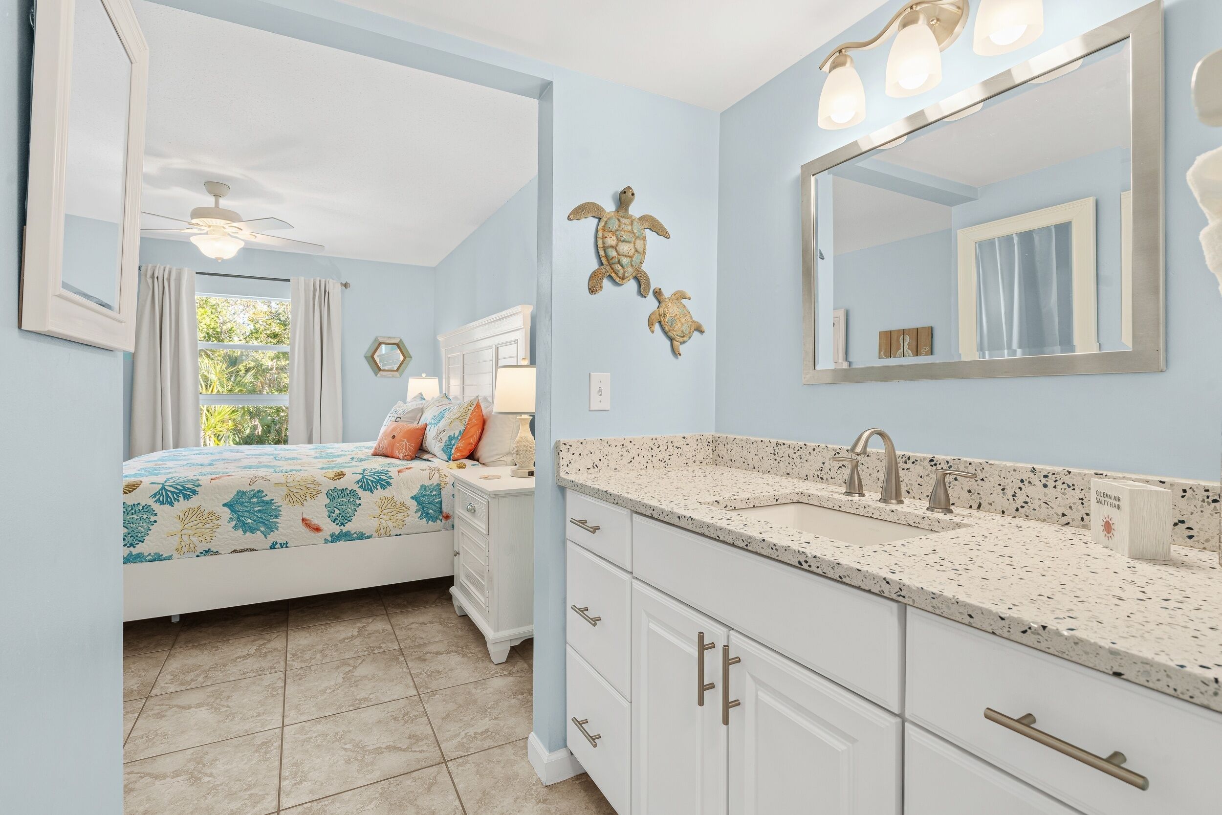 A bedroom with a bed, nightstand, dresser, and a bathroom with a sink and mirror.