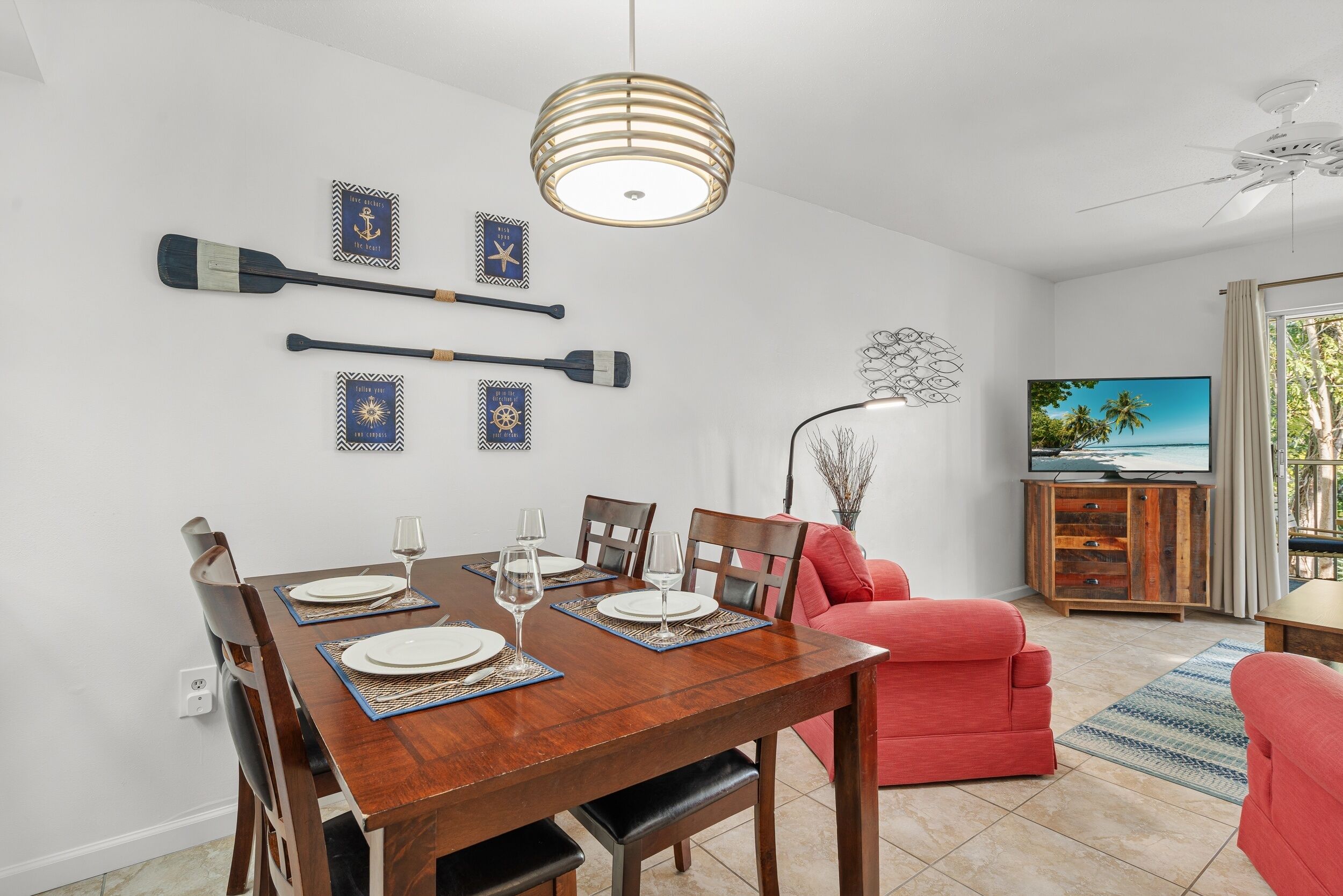 A dining area with a wooden table set for four, a red sofa, a TV, and decorative wall art.