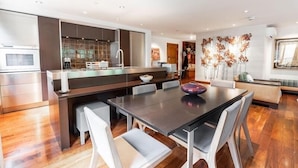 A modern kitchen with a central island, a dining area with a dark table and white chairs, and a living area with a sofa and decorative wall art. - Riverhouse #3 2 Bedroom Condo by RedAwning (Vail)
