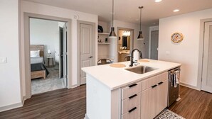 A modern kitchen with a central island, pendant lighting, and a visible clock on the wall.