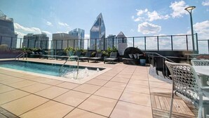 A rooftop pool with a city skyline view, lounge chairs, and a barbecue area.