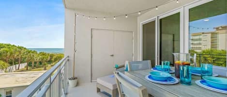 A balcony with a dining table set for four, overlooking a beach and ocean.