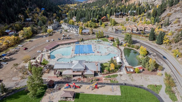 A resort with a large swimming pool, a children's play area, and a road curving through the landscape. - Main Level Haven | Steps from the Hot springs | Sleeps 9 (Ouray)