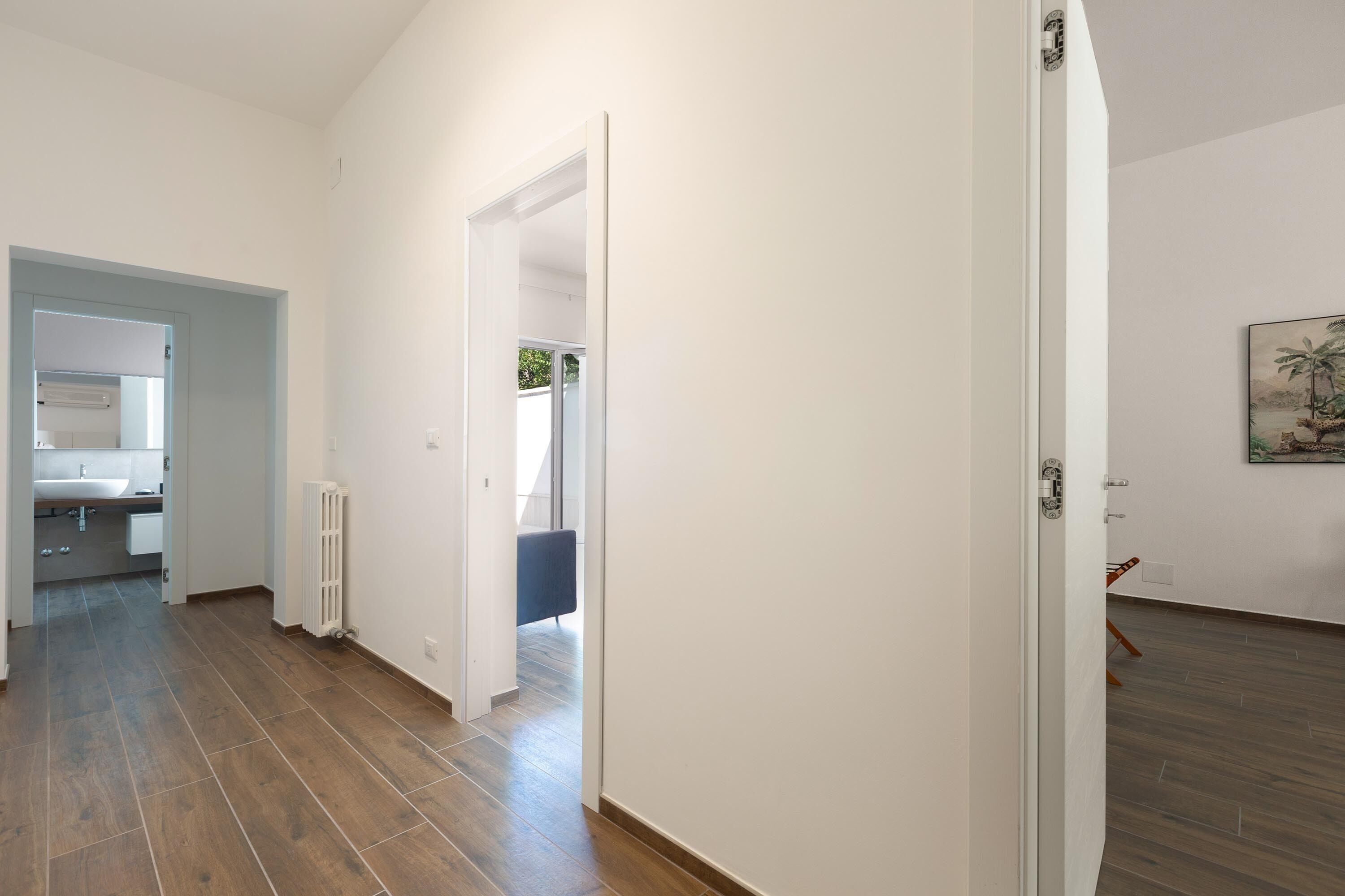 Un pasillo con suelo de madera, una puerta blanca y vista a una habitación con una silla azul.