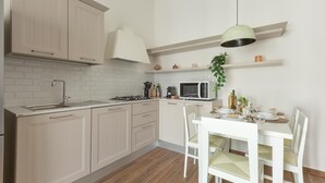A modern kitchen with white cabinets, a microwave, and a dining area with white chairs. - 3624 Casa di Rosa - Ionio by Barbarhouse (Maglie)