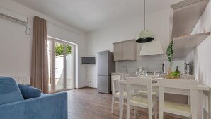A modern kitchen with white cabinets, a dining table with chairs, a refrigerator, and a TV mounted on the wall. - 3624 Casa di Rosa - Ionio by Barbarhouse (Maglie)