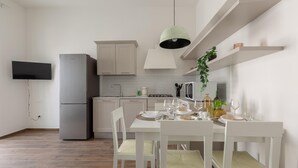 A modern kitchen with white cabinetry, a grey refrigerator, a dining table set with plates and glasses, and a hanging light fixture. - 3624 Casa di Rosa - Ionio by Barbarhouse (Maglie)