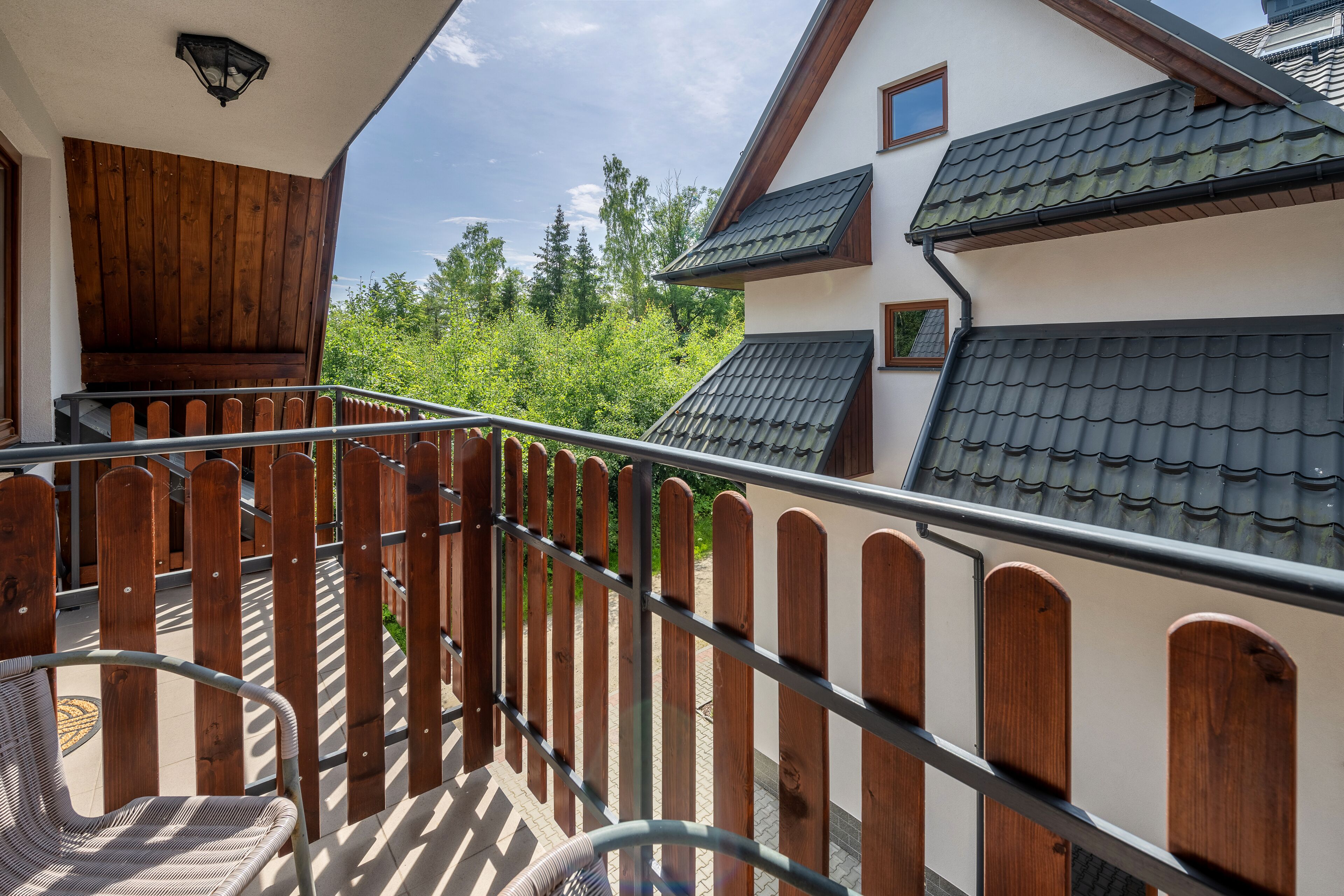 A balcony with a wooden fence, a wicker chair, and a view of a house with a tiled roof.