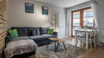 A modern living room with a grey sofa, a small round table, and a dining area with a white table and chairs.