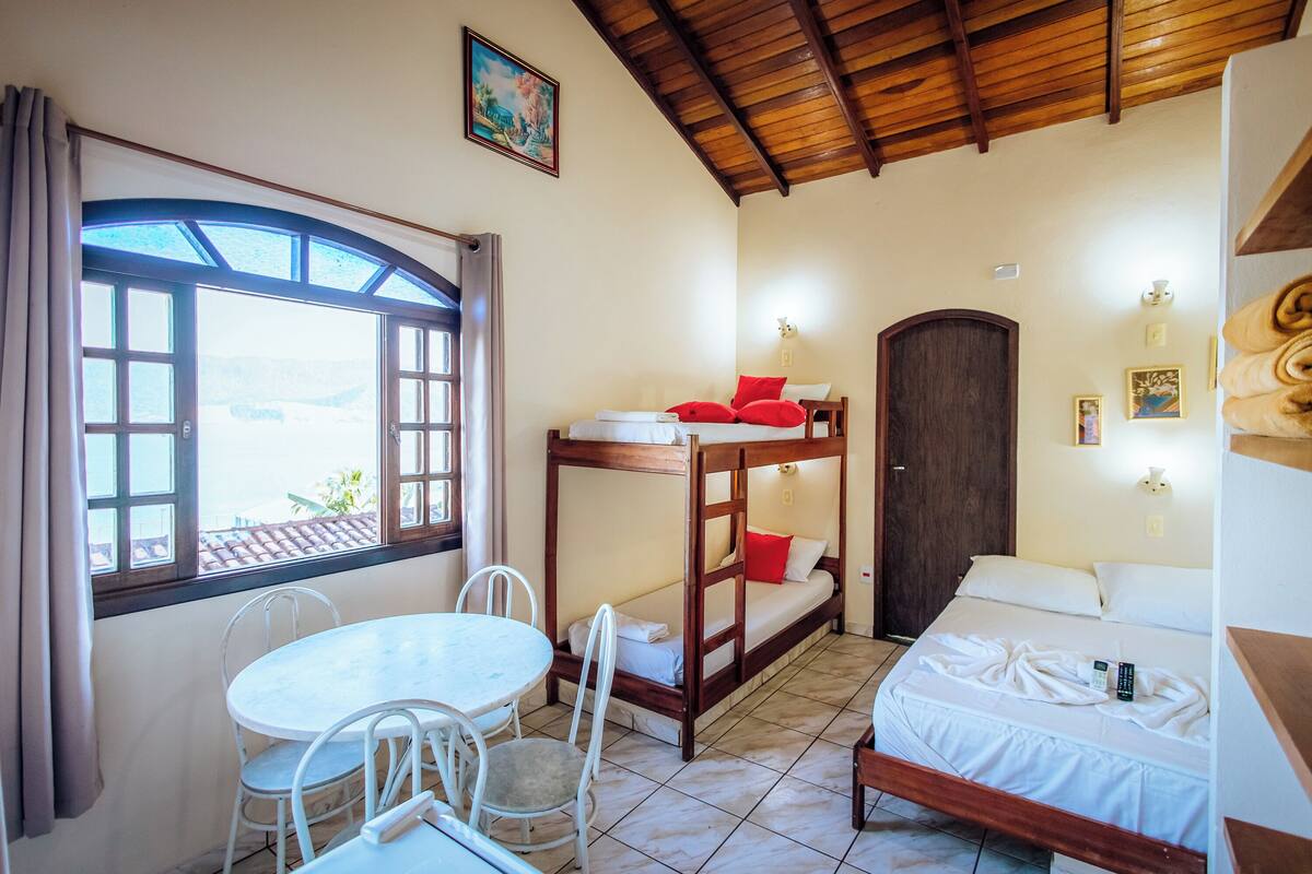 A room with a bunk bed, a small table with chairs, a window with curtains, and a door.