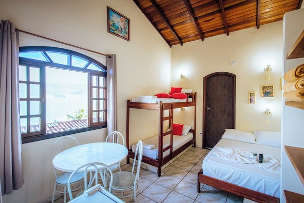 A room with a bunk bed, a small table with chairs, a window with curtains, and a door.