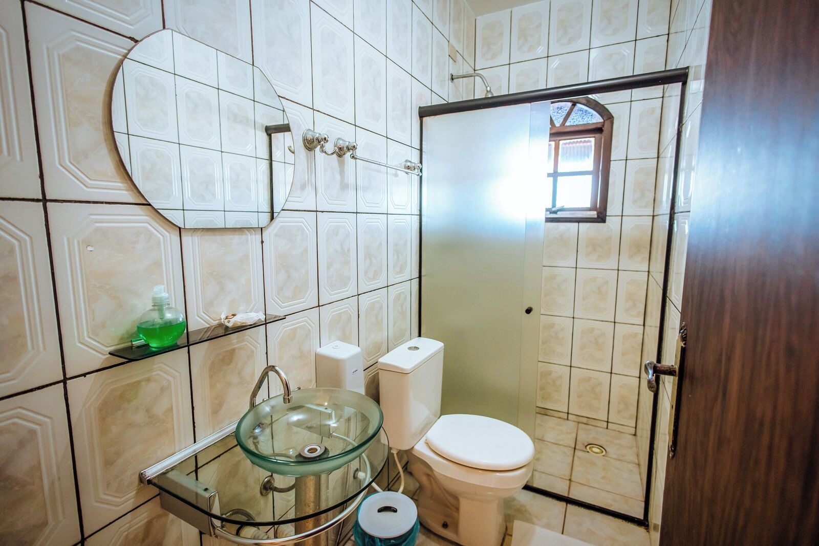 Un baño con lavamanos de vidrio, inodoro y zona de ducha.
