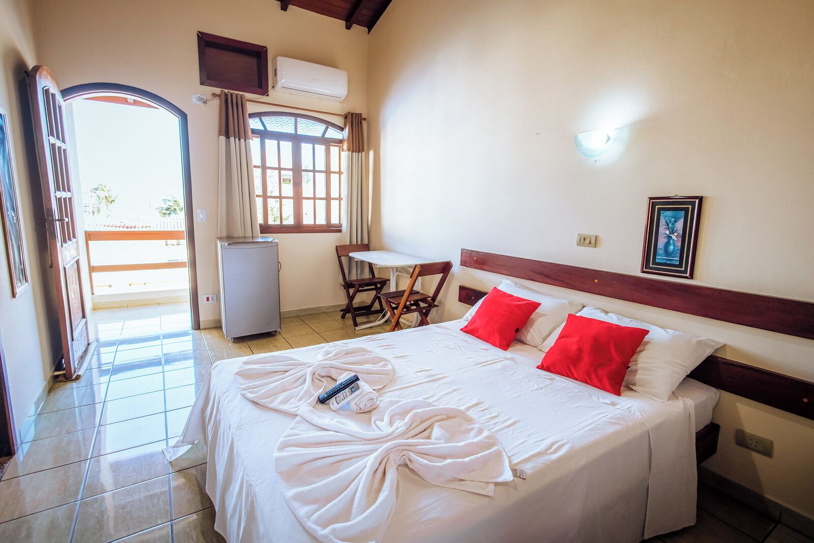 Habitación de hotel con cama, escritorio, silla, refrigerador y ventana con cortinas.