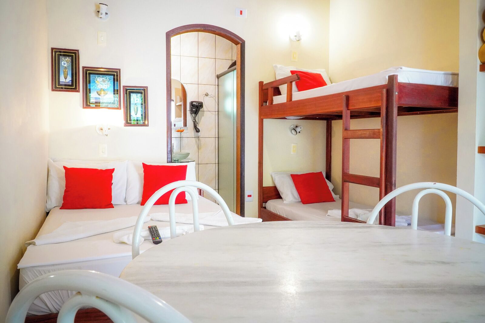 A room with bunk beds, a table, and chairs. There are framed pictures on the wall.
