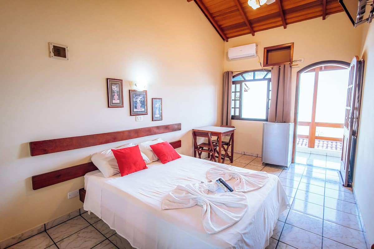 A hotel room with a bed, a small table, a chair, and a balcony with a view.