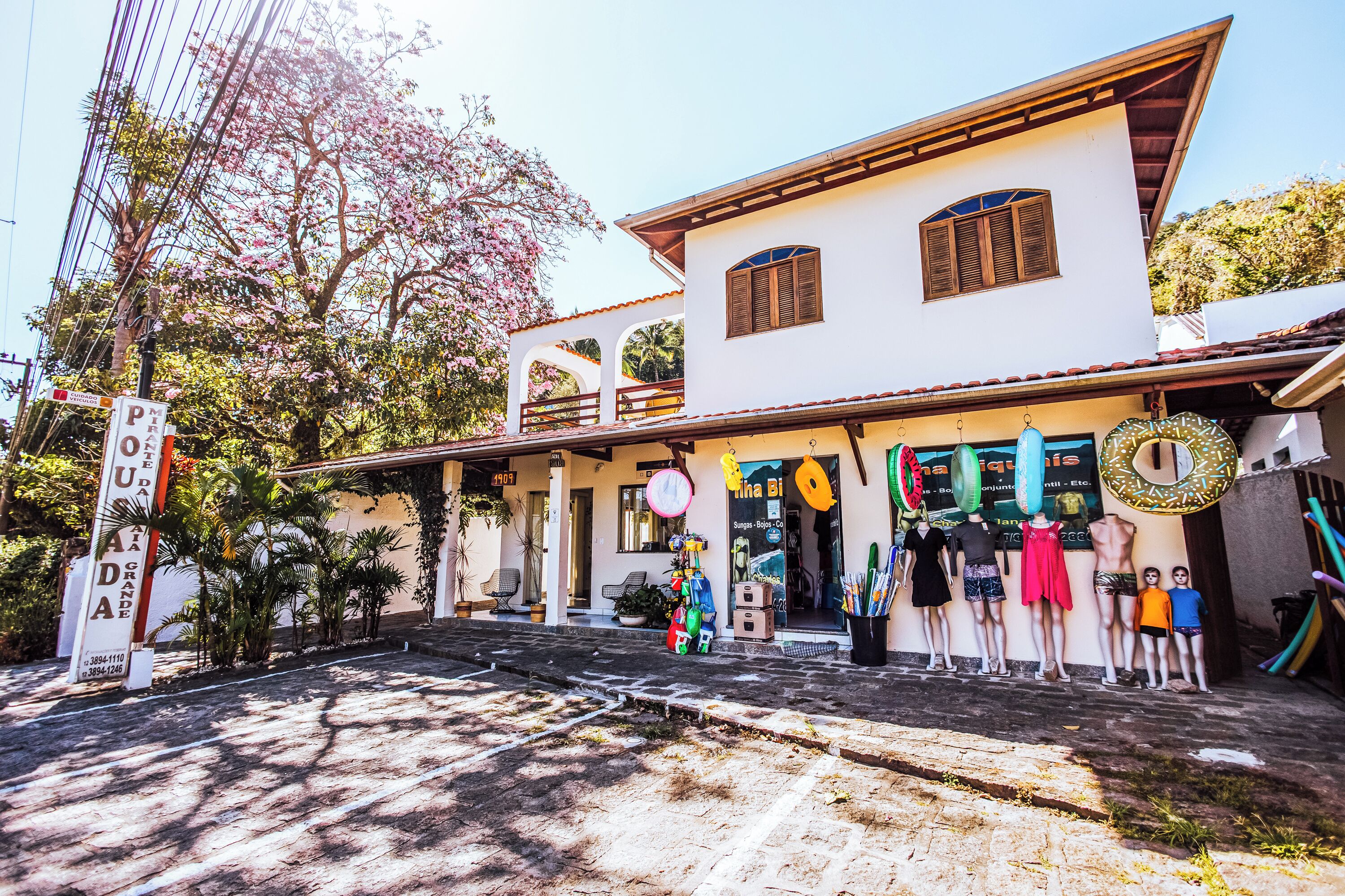 Edifício de dois andares com fachada branca e telhado de telhas. Manequins exibem diferentes roupas na parte externa.