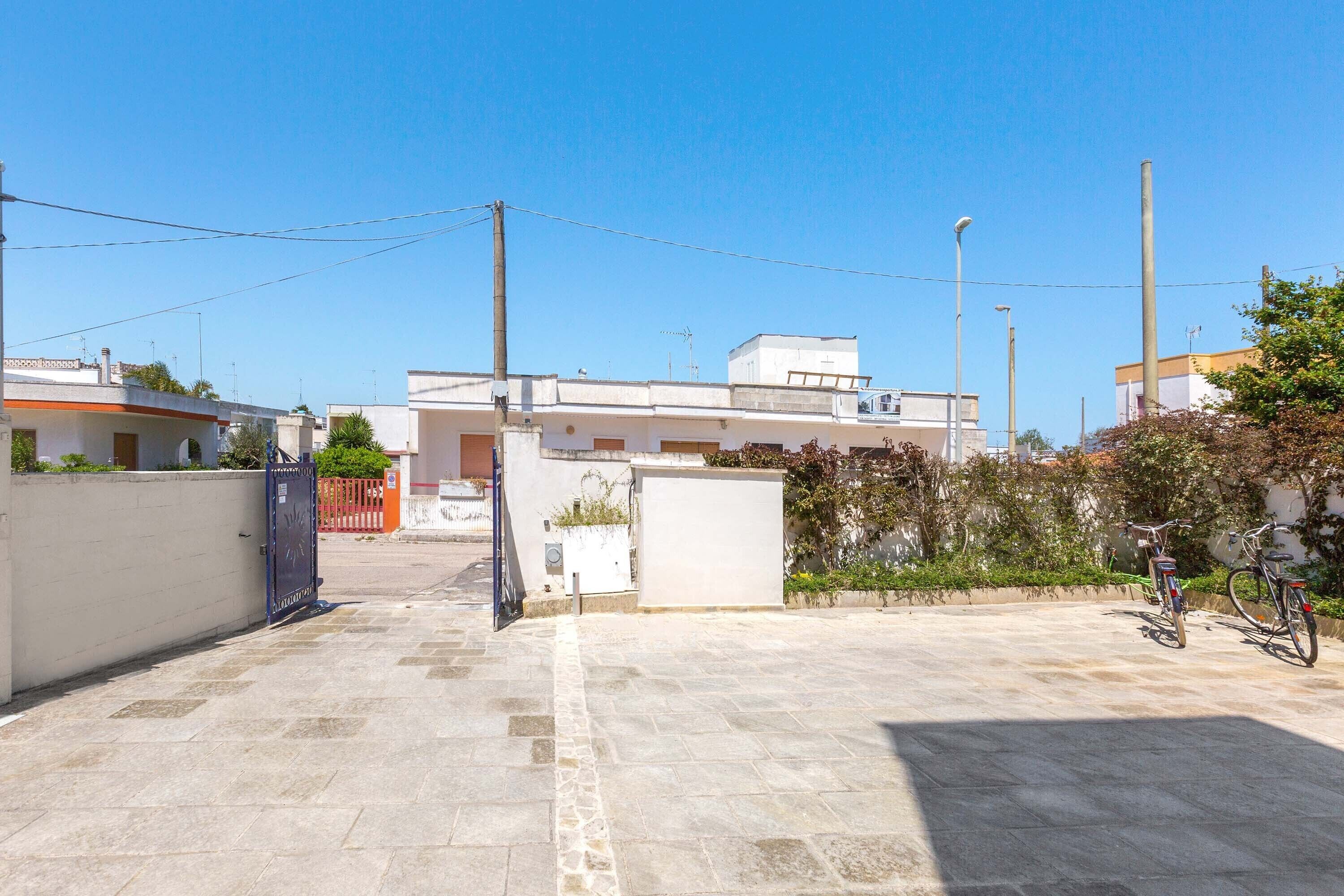 A courtyard with a paved floor, a gate, and a building with a flat roof in the background.