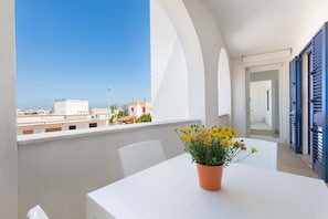 Ein Balkon mit einem weißen Tisch und Stühlen, einem Blumentopf und Blick auf Gebäude.